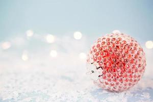 Red Christmas ball on a blue background with artificial snow and lights of garlands in bokeh. Festive background, new year. Copy space photo