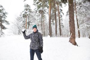 un joven con una bola de nieve en la mano se está divirtiendo, balanceándose para lanzar. juegos familiares y amistosos de invierno y entretenimiento en el bosque con nieve al aire libre foto