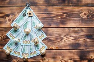 Christmas tree made of 100 dollar bills on wooden background with copyspace and House key. Christmas decor of finance, savings, wealth, expenses in new year. Real estate, housing, mortgage, relocation photo