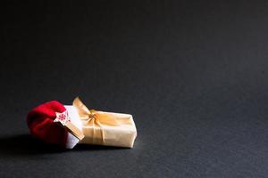 A box with a Christmas gift in a package tied with a ribbon and with a Santa hat on a black background. Black Friday, buying gifts for the new year. Space for text photo