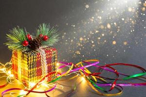 Christmas gift box on a black background with a garland and serpentine in the glitter. Decorated with fir branch with berries and cones, wrapped in a knitted warm wrapper. New Year. Copy space photo