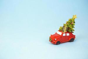 Christmas decor - a red retro car carries a Christmas tree with gift boxes on the roof. Toy with sequins on a blue background, space for text. New Year photo