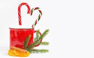 A red mug with marshmallows and candy cane in the shape of a heart is decorated with a natural fir branch or dried orange slices and cinnamon sticks. Christmas and New Year, the flavor of the holiday photo