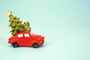 Christmas decor - a red retro car carries a Christmas tree with gift boxes on the roof. Toy with sequins on a blue background, space for text. New Year photo