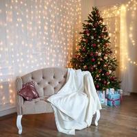 Decorated Christmas tree in the living room with sofa, blanket, lights garlands. Bedroom with a bed. New year, Christmas photo
