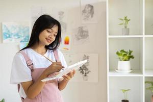 Young girl standing on the floor and hold Color palette and brush at room. Hobby and art study at home. photo