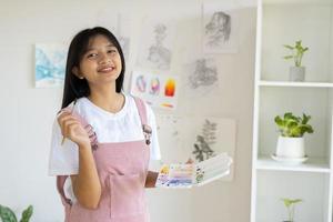 Young girl standing on the floor and hold Color palette and brush at room. Hobby and art study at home. photo