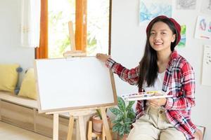 niña sentada en una silla con caballete para dibujar paleta de colores y pincel en la habitación. foto