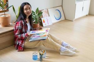 niña sentada en el suelo y pintando sobre papel en casa. hobby y estudio de arte en casa. foto