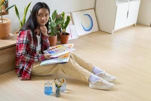 Young girl sitting on the floor and painting on paper at home. Hobby and art study at home. photo