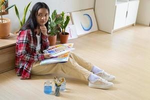 niña sentada en el suelo y pintando sobre papel en casa. hobby y estudio de arte en casa. foto