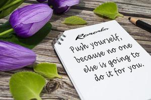 Motivational quote on notepad with flowers on wooden desk. photo