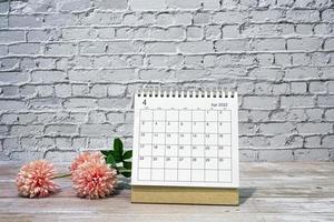 April 2022 white calendar with flowers on wooden desk. Copy space. photo