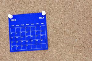 May 2023 blue calendar with pin on cork bulletin billboard. photo