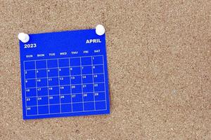 April 2023 blue calendar with pin on cork bulletin billboard. photo