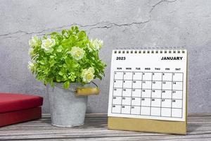 calendario de escritorio de enero de 2023 en escritorio de madera con planta en maceta y libros. foto