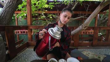 thee ceremonie uitgevoerd door een jong brunette vrouw Aan buitenshuis terras video