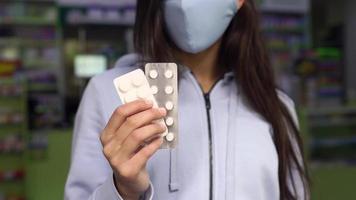 Woman wearing a mask holds and show medication at pharmacy video