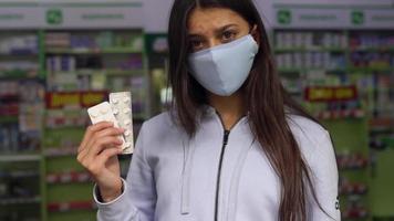 Woman wearing a mask holds and show medication at pharmacy