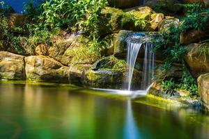 Japanese garden waterfalls. Lush green tropical Koi pond with waterfall from each side. A lush green garden with waterfall cascading down the rocky stones. Zen and peaceful background. photo