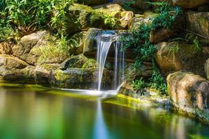 Japanese garden waterfalls. Lush green tropical Koi pond with waterfall from each side. A lush green garden with waterfall cascading down the rocky stones. Zen and peaceful background. photo