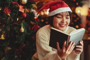 a young Woman in front of Christmas tree reading a book at home with x-mas decoration. photo