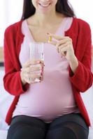 mujer embarazada sosteniendo un vaso de agua y tomando pastillas en la mano para alimentar su cuerpo. foto