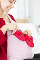 una gran mujer embarazada juega alegremente con los zapatos del bebé en su estómago. foto
