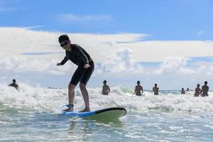 A young boy wearing swimming goggles stands on a soft board while practicing surfing in a beginner's class. photo