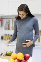 una mujer hermosa, fresca y embarazada parada en una cocina moderna comiendo una ensalada saludable. nueva mamá comiendo alimentos orgánicos para una buena salud foto