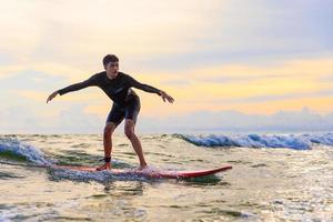 Young teen boy surfer riding waves on soft board in Rayong beach, Thailand. Rookie teenager surfboard student playing on water in excited and funny action. photo