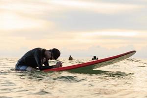 Young boy teenager surfboarder bows his head in exhaustion, tired, and disappointment during learning and practicing surfing. photo