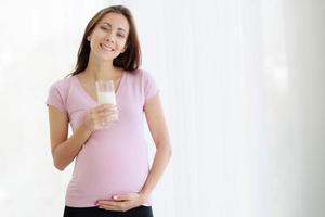 Beautiful, cheerful, pregnant woman holds glass of milk to nourish the body and the unborn. photo