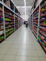 Jombang, East Java, Indonesia, 2022 -  a quiet shop aisle with rows of shelves filled with colorful household items or utensils retail, photo