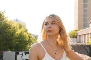 mujer rubia feliz en la calle de la ciudad con edificios antiguos y árboles. foto