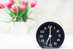 Black alarm clock and flower in vase on table photo