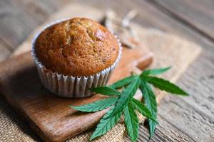 pastel de comida de cannabis con hierba de marihuana de hoja de cannabis sobre fondo de madera, deliciosos cupcakes dulces de postre con planta de hoja de cáñamo, tentempié de comida de hierbas cbd y concepto médico foto