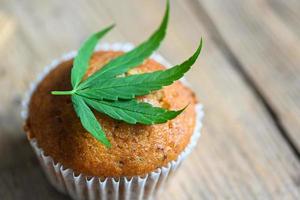 pastel de comida de cannabis con hierba de marihuana de hoja de cannabis sobre fondo de madera, deliciosos cupcakes dulces de postre con planta de hoja de cáñamo, tentempié de comida de hierbas cbd y concepto médico foto