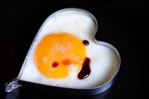 huevos fritos en una sartén con salsa para el desayuno en un fondo negro - huevo frito para un corazón sano y un concepto de cocina de amor mental foto