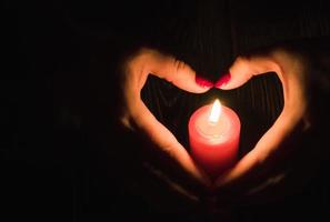 manos femeninas sosteniendo una vela encendida en la oscuridad, forma de corazón foto