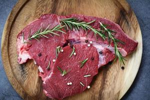 Raw beef meat rosemary on wooden cutting board on the kitchen table for cooking beef steak roasted or grilled with ingredients herb and spices Fresh beef animal protein photo