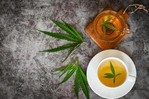 té de cannabis a base de hierbas en una taza de té con hoja de cannabis hojas de marihuana hierba sobre fondo oscuro, té de salud con planta de hoja de cáñamo thc cbd hierbas alimentos y medicina foto