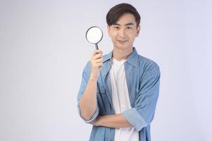 Young asian man holding magnifying glass over white background, analysis and finance concept. photo