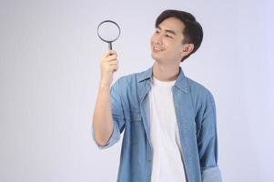 Young asian man holding magnifying glass over white background, analysis and finance concept. photo