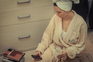 Young woman in bathrobe texting on cell phone in the evening. photo