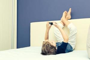 Small boy taking selfie with cell phone while lying on the bed. photo