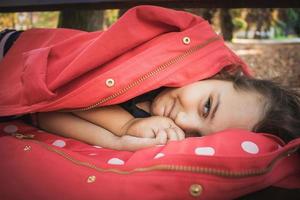 linda chica sonriente envuelta en una chaqueta relajándose en un banco del parque. foto