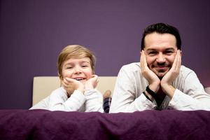 Happy son and father lying down on bed and looking at camera. photo