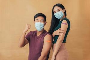 Asian man and woman showing shoulders after getting a vaccine. Happy couple showing arm with band-aids on after vaccine injection. photo