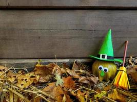calabaza de halloween divertida verde con ojos de gafas en sombrero de fieltro de bruja verde, su escoba amarilla está cerca. antiguo fondo de pared de madera oscura con espacio de copia. foto